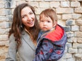 Baby with mom on a brick background. looking at the camera in warm clothes. Happy and young mother sitting on brick background and Royalty Free Stock Photo