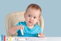 A baby of 12-17 months draws with felt-tip pens sitting on a child`s chair Royalty Free Stock Photo