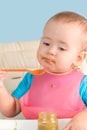 A baby of 12-17 months holding a spoon in his hand eats vegetable mashed broccoli from a glass jar, vertical photo Royalty Free Stock Photo