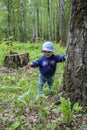 Baby 8-9 months learns to walk, walks through the woods holding a tree trunk. Little girl smiling on a walk in the park Royalty Free Stock Photo