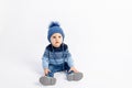 Baby 8 months old boy sitting on a white isolated background in warm winter clothes and a hat, children`s fashion, advertising Royalty Free Stock Photo