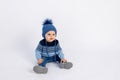 Baby 8 months old boy sitting on a white isolated background in warm winter clothes and a hat, children`s fashion, advertising Royalty Free Stock Photo