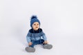 Baby 8 months old boy sitting on a white isolated background in warm winter clothes and a hat, children`s fashion, advertising Royalty Free Stock Photo