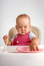 A baby 12-15 months old sits on a feeding chair and reaches into a plate of food with his hand, vertical photo Royalty Free Stock Photo