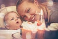 Baby with mother looking at birthday cake with candle during celebration first birthday