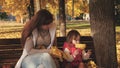 Baby and mother play with autumn maple leaves. little daughter and mother play in autumn Park on bench. concept of happy