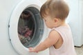 Baby near washing machine, having fun and playing with washer