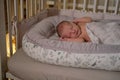 A baby newborn is sleeping in a baby cocoon with a burning night light. A child is an infant in a home crib by the light of a Royalty Free Stock Photo