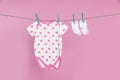 Baby onesie and socks drying on laundry line against pink background Royalty Free Stock Photo