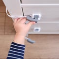 Baby opens the child lock on the closed drawer of the cabinet. Toddler