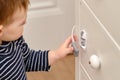 Baby opens the child lock on the closed drawer of the cabinet. Toddler