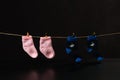 Baby Pink and blue socks hang on a pin on a rope. Shadow below. On a black background Royalty Free Stock Photo