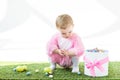 Baby in pink fluffy costume sitting on green grass near gift box with pink bow and colorful Easter eggs isolated on Royalty Free Stock Photo