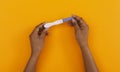 Black female hands holding blank pregnancy test over orange background