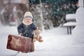 Baby playing with teddy in the snow, winter time. Little toddler boy in blue coat, holding suitcase and teddy bear, playing Royalty Free Stock Photo