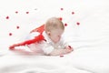 A baby with plump cheeks in white clothes with red cupid wings, lies on his stomach, plays with a heart Royalty Free Stock Photo