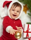 Baby portrait in christmas decoration, dressed as Santa, lie on fur near fir tree and play with gifts, winter holiday concept Royalty Free Stock Photo