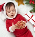 Baby portrait in christmas decoration, dressed as Santa, lie on fur near fir tree and play with gifts, winter holiday concept Royalty Free Stock Photo