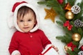 Baby portrait in christmas decoration, dressed as Santa, lie on fur near fir tree and play with gifts, winter holiday concept Royalty Free Stock Photo