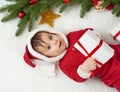 Baby portrait in christmas decoration, dressed as Santa, lie on fur near fir tree and play with gifts, winter holiday concept Royalty Free Stock Photo