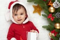 Baby portrait in christmas decoration, dressed as Santa, lie on fur near fir tree and play with gifts, winter holiday concept Royalty Free Stock Photo