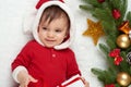 Baby portrait in christmas decoration, dressed as Santa, lie on fur near fir tree and play with gifts, winter holiday concept Royalty Free Stock Photo