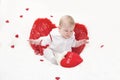 A baby with puffy cheeks in white clothes with red cupid wings with closed eyes, sits with arms spread apart, flies