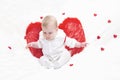 A baby with puffy cheeks in white clothes with red cupid wings with, sits with arms spread apart, flies