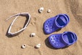 Baby purple clog and sunglasses on the sand on the beach. Cute details of summer holidays. Baby shoes on the beach. Royalty Free Stock Photo