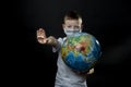 Baby reaches forward hand STOP, NO. Boy is holding a globe, a model of the planet Earth. Boy is careful of the virus. Coronavirus
