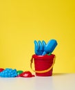 Baby red plastic bucket with shovel and toys on a yellow background Royalty Free Stock Photo