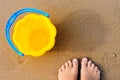 Baby`s bare feet on a golden sandy beach next to a yellow toy bucket. Vacation concept Royalty Free Stock Photo