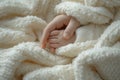 Baby\'s hand grasped by mother hand on a white knitted blanket. Symbolizing parental care, love, and protection