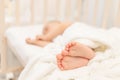 Baby`s legs in focus against the background of a sleeping baby in a white bed, a healthy and calm baby`s sleep Royalty Free Stock Photo