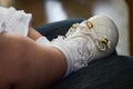 A baby's little foot, dressed in white socks, with lace ruffles, a little white shoe, round toe, bow with gold detail