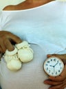 Baby`s shoes, pregnant belly and ticking clock