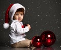 Baby in Santa hat with xmas tree ball on snowfall background