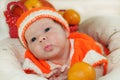 Baby sending air kiss. Portrait of newborn baby in orange knitted costume on white blanket and basket with oranges and pumpkin be