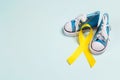 Baby shoes with childhood cancer awareness golden ribbon on blue background with copy space Royalty Free Stock Photo