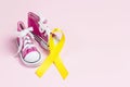 Baby shoes with childhood cancer awareness golden ribbon on pink background with copy space Royalty Free Stock Photo