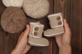 Baby shoes in woman hands, yarn balls on woodenbackground.