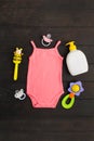 Baby shower accessories. Pink summer bodysuit, two sylicone pacifiers and two wooden and plastic rattles on wooden background with Royalty Free Stock Photo