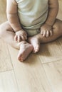 Baby sits on a wooden laminate floor. Bare legs and feet of a baby in the living room floor Royalty Free Stock Photo