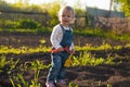 Baby sitting on the ground with shovel and rake in sunlight. Cute summer blond girl in the garden Royalty Free Stock Photo