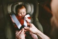 Baby sitting in safety car seat and father fastens belt