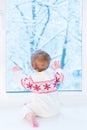 Baby sitting at window watching snow covered trees Royalty Free Stock Photo