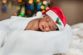 A baby sleeping comfy in blanket and Santa hat under colourful Christmas lights Royalty Free Stock Photo