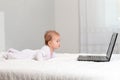 Baby in sliders lies on the bed and looks at the laptop. Side view. Copy space. The concept of teaching children to modern Royalty Free Stock Photo