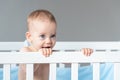 Baby with a sly expression on the face of a little prankster in a white classic crib