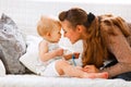 Baby with soother and young mom playing on divan